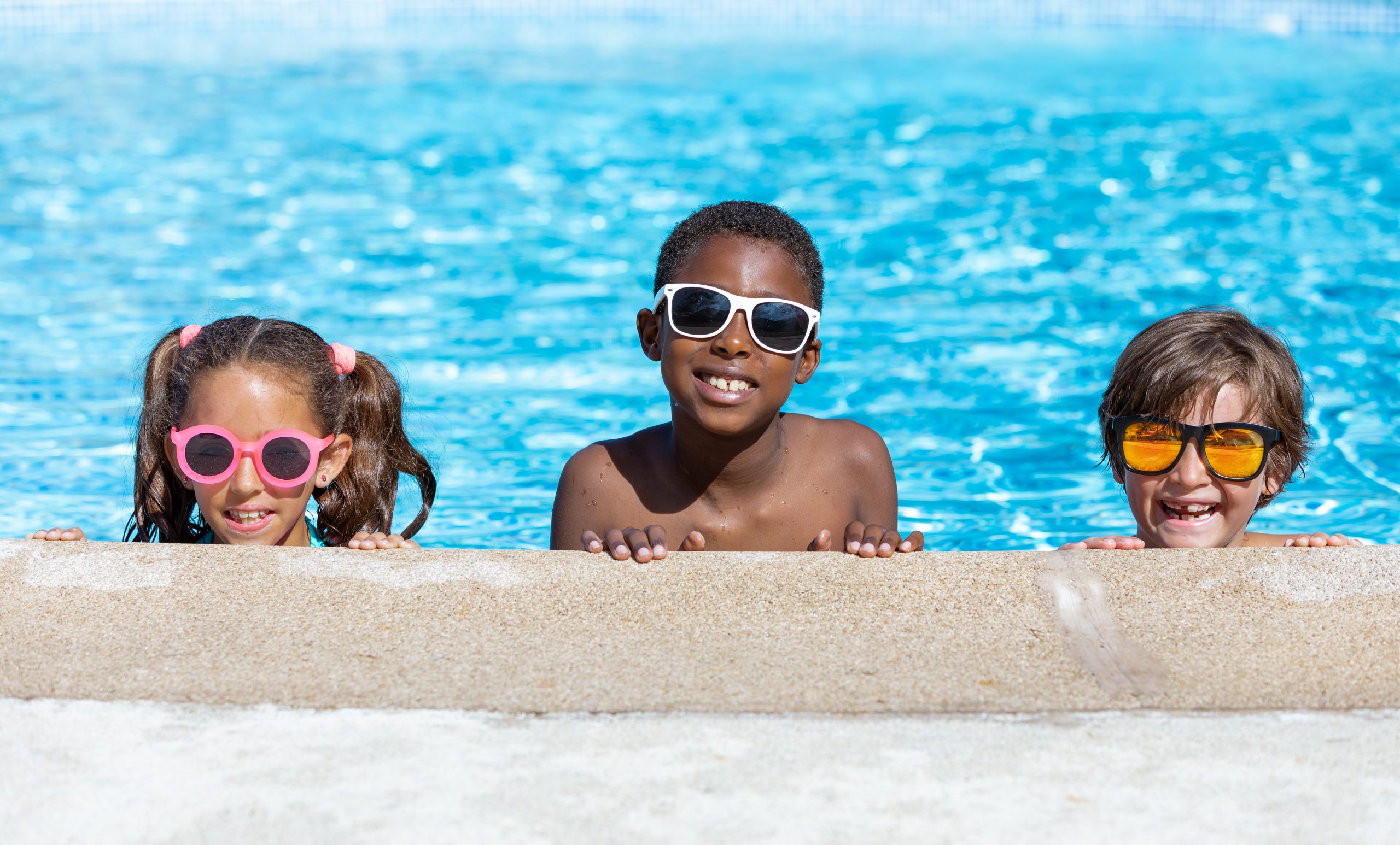 Three kids wearing sunglasses in a pool.