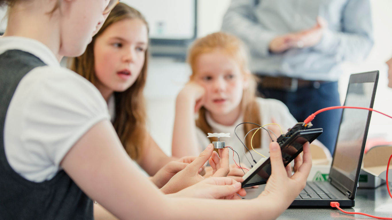 Female students are following instructions on a laptop to make a propeller spin by building an electrical circuit as part of their school energy review.