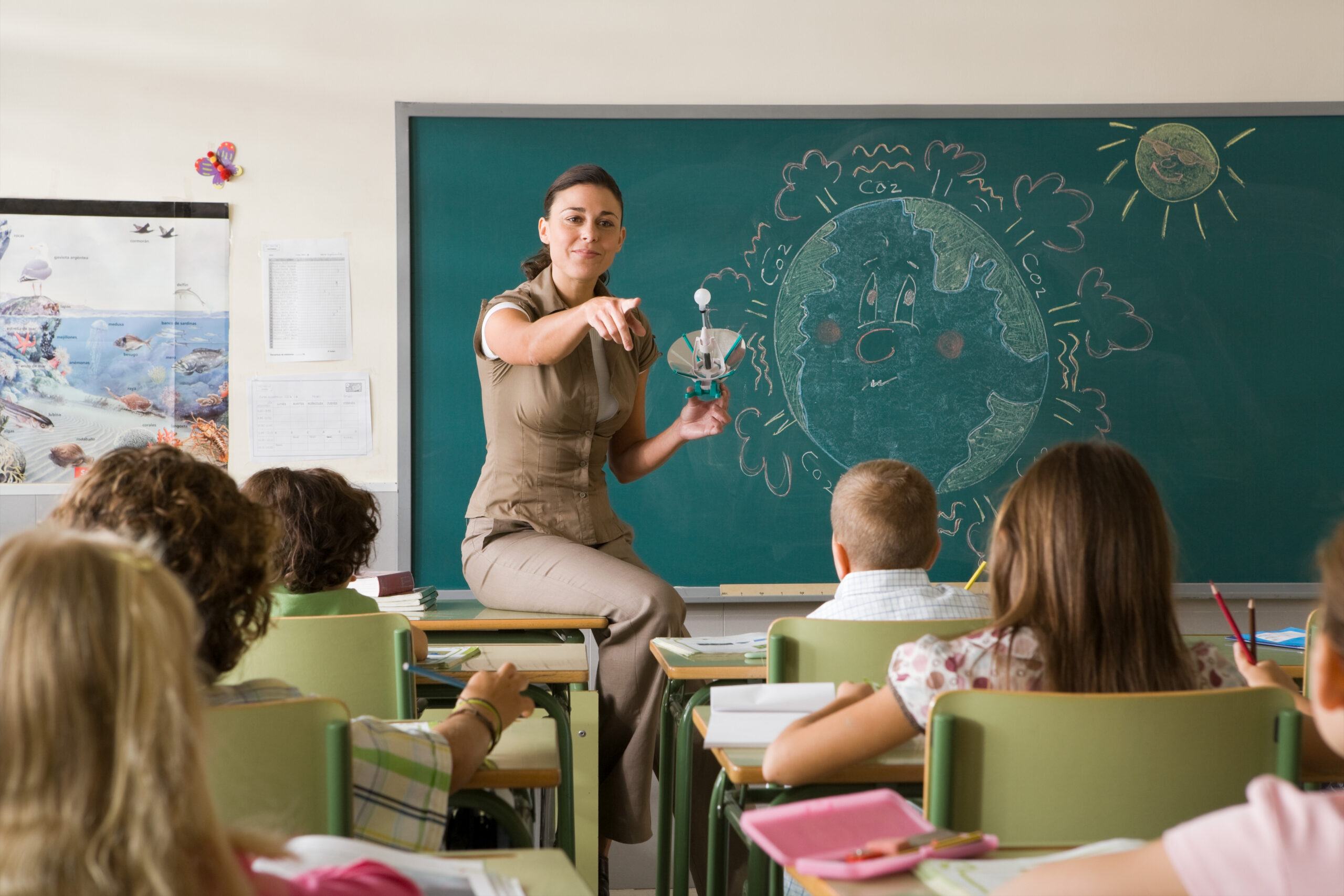 teacher sitting on student's desk pointing to the classs